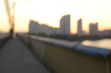 Köprü ve günbatımı görüntüsü çözüldü. Nehir üzerinde binalar var.