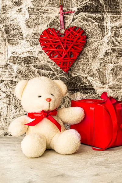 White Teddy bear with red heart and gift box on grey wall background. Rattan work of heart shape