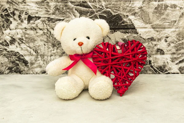 White Teddy bear with red heart on grey wall background. Rattan work of heart shape