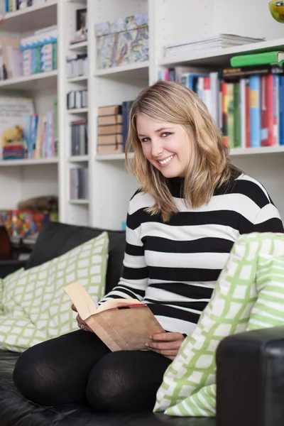 Young, attractive woman sits on the couch and reads a book — Stock Photo, Image