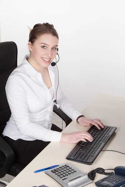 Young woman with headset types at the keyboard — Stock Photo, Image