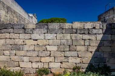 Doku, arka plan, desen. Kadim kuru taş duvar. Zamanla kırılmış ve mahvolmuş düzensiz taşlar. Yabani otlar azalır. Sert ve kirli yüzey.