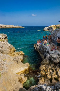 17 Ağustos 2021 - Otranto, Puglia, İtalya - Porto Badisco 'nun küçük plajı, ünlü sahil beldesi Salento. Turistler yaz tatillerini geçirirler. İnsanlar eğleniyor ve denizde yüzüyor..