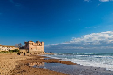 Santa Marinella, Roma, Lazio, İtalya soğuk bir kış gününde Santa Severa 'nın deniz kenarındaki şatosu. Dalgalı deniz, güçlü rüzgar, bulutlu mavi gökyüzü. Birçok insan sahilde gezer ve güneşin tadını çıkarır..