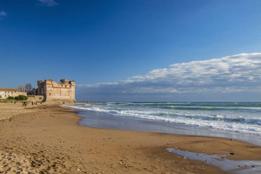 Santa Marinella, Roma, Lazio, İtalya soğuk bir kış gününde Santa Severa 'nın deniz kenarındaki şatosu. Dalgalı deniz, güçlü rüzgar, bulutlu mavi gökyüzü. Birçok insan sahilde gezer ve güneşin tadını çıkarır..
