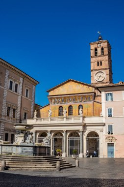 Trastevere 'deki Santa Maria Bazilikası, Roma' nın merkezinde bir meydanda. Portico ve mozaikli cephe, saatli çan kulesi ve yazıtlı çeşme..