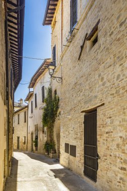 19 Haziran 2022 - Perugia, Umbria, İtalya. Ortaçağ köyü Bevagna 'da karakteristik bir ara sokak. Güneşli bir yaz gününde, binaların arasında mavi gökyüzü. Taş ve tuğla duvarlar. 
