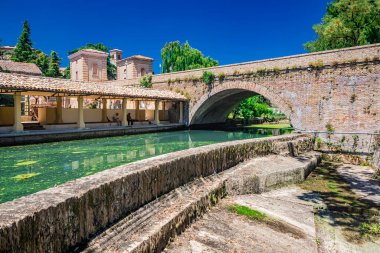 June 19, 2022 - Perugia, Umbria, Italy. The ancient wash-house and the masonry bridge over the river, in the medieval village of Bevagna. Green algae on the surface of the stagnant water.