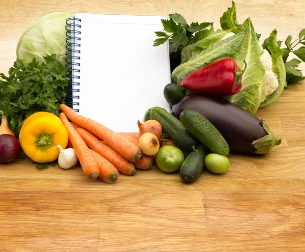 Assortiment van verse groenten en lege receptenboek — Stockfoto
