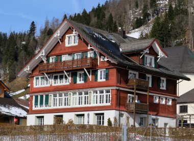 Geleneksel İsviçre mimarisi ve tahtadan dağ evleri ilkbahar aylarının başlarında ve etrafındaki çayırlarda kar kalıntılarıyla, Wildhaus - Obertoggenburg, İsviçre (Schweiz)