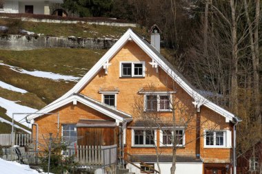 Geleneksel İsviçre mimarisi ve tahtadan dağ evleri ilkbahar aylarının başlarında ve etrafındaki çayırlarda kar kalıntılarıyla, Wildhaus - Obertoggenburg, İsviçre (Schweiz)