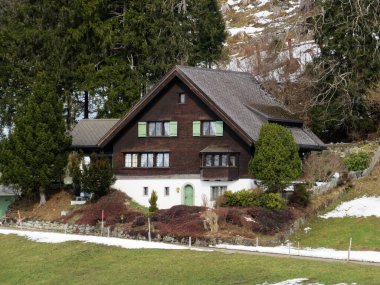 Geleneksel İsviçre mimarisi ve tahtadan dağ evleri ilkbahar aylarının başlarında ve etrafındaki çayırlarda kar kalıntılarıyla, Wildhaus - Obertoggenburg, İsviçre (Schweiz)