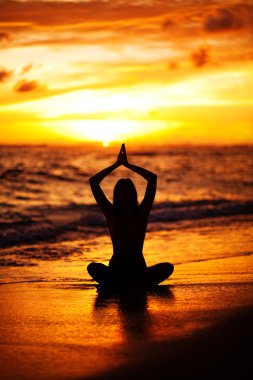 lotus pozisyonda okyanusun kıyısında yoga yaparken oturan genç kadın