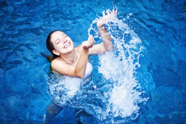 Young beautiful woman splashing water in swimming pool clipart