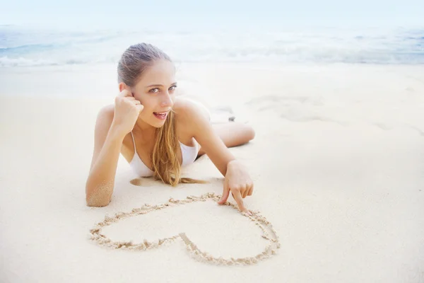 Liefde concept: jonge mooie vrouw op het strand maken van hart op het zand — Stockfoto