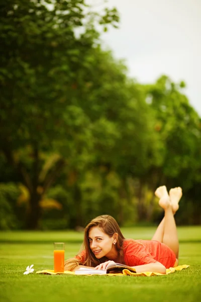 Jonge vrouw op het gras met boek en sinaasappelsap — Stockfoto