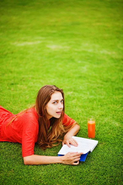 Mladá žena v trávě s knihu a pomerančový džus — Stock fotografie