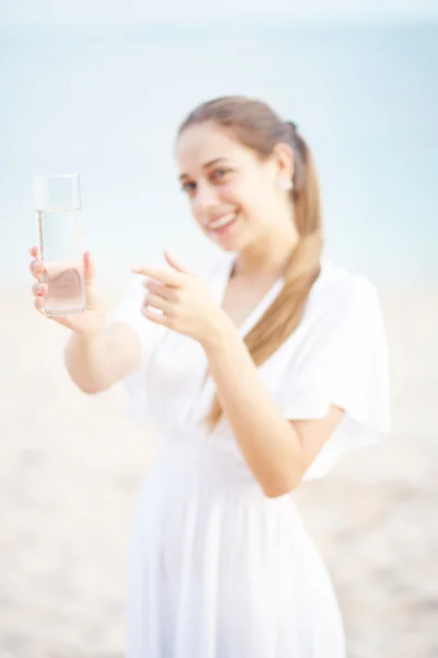 Ung kvinna på havet stranden i vit klänning med glas vatten — Stockfoto