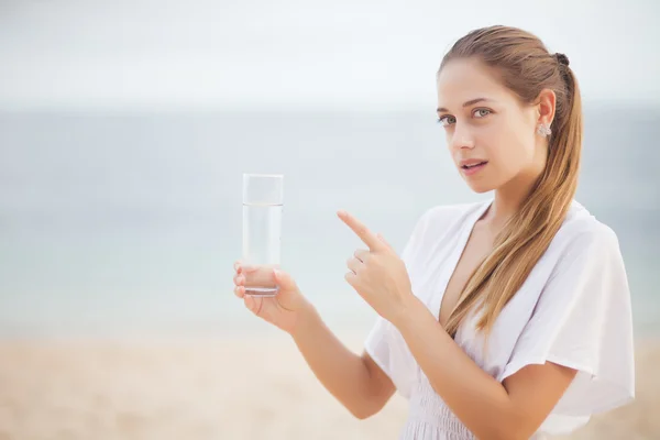 Fiatal nő fehér ruhában pohár vízzel óceán partján — Stock Fotó