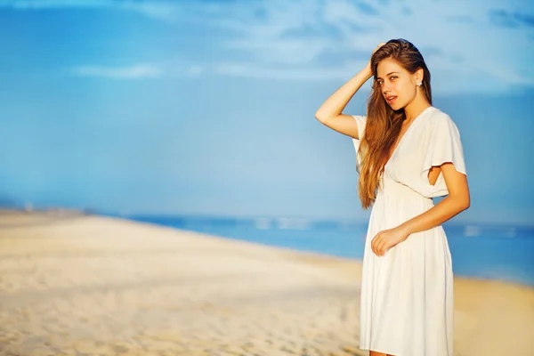 Jonge vrouw aan de oever van de Oceaan in witte jurk — Stockfoto