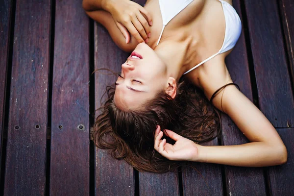 Молодая женщина в купальнике лежит на деревянном полу под открытым небом — стоковое фото