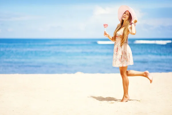 San Valentino: Giovane donna caucasica con in mano un lecca-lecca-cuore sulla spiaggia — Foto Stock