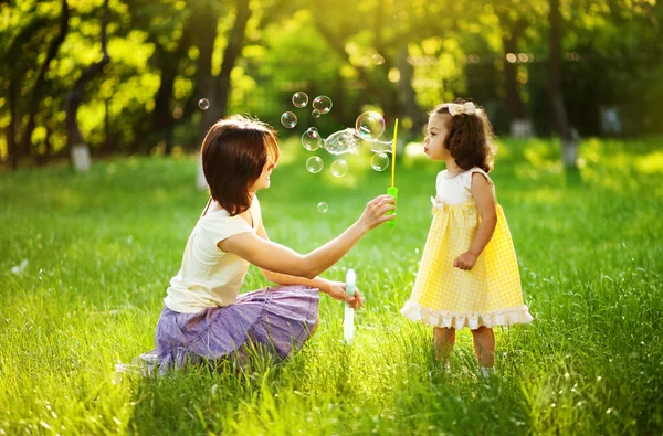 Glückliche junge Mutter und ihre Tochter pusten Seifenblasen im Park — Stockfoto