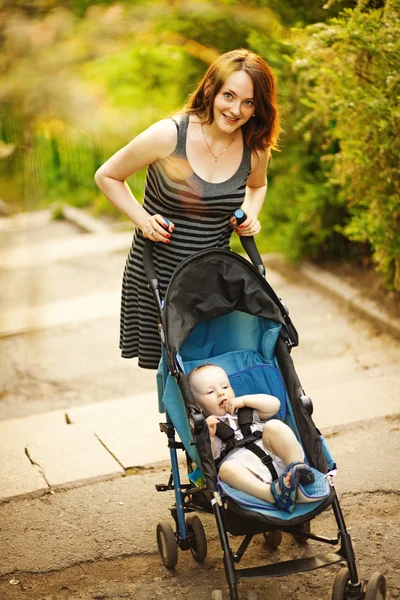 Jovem mãe feliz com bebê no buggy andando no parque — Fotografia de Stock