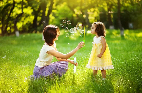 Glückliche junge Mutter und ihre Tochter pusten Seifenblasen im Park Stockbild