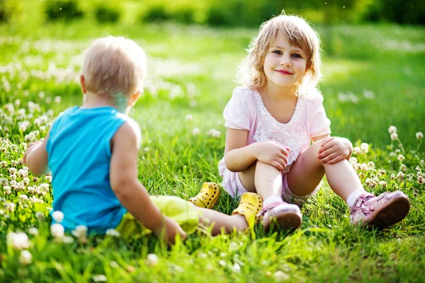 Two children are sitting on green meadow and smile Stock Photo