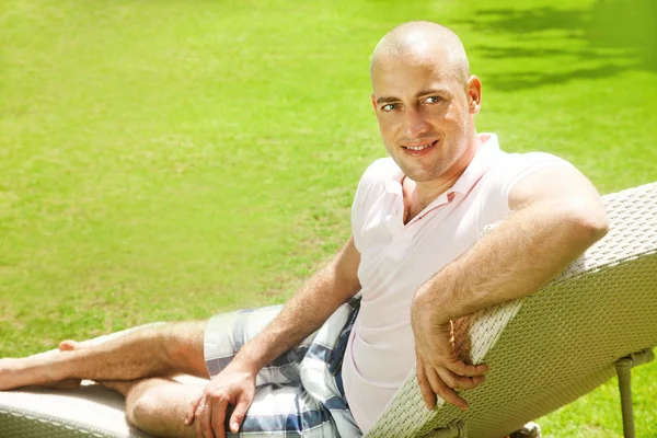 Homem adulto em roupas casuais sentado em uma cadeira de praia em um prado florido e um descanso — Fotografia de Stock
