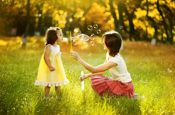 Gelukkig jonge moeder en haar dochter blazen van zeepbellen in de herfst — Stockfoto