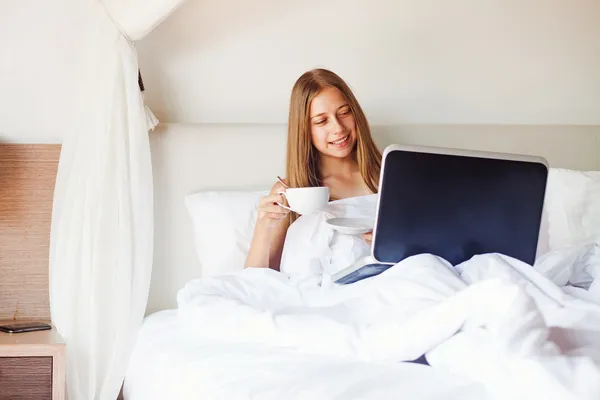 Schöne Frau in hellem Interieur mit Laptop und Tee oder Kaffee trinken — Stockfoto