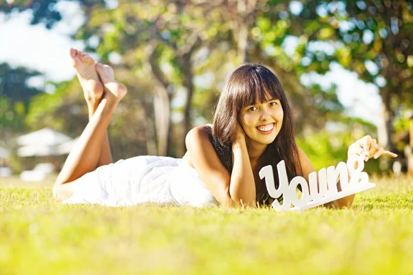 Woman on the grass with the word "young" in her hands — Stock Photo, Image