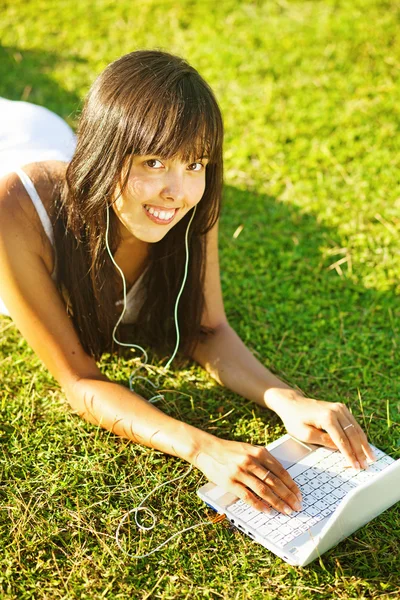 Mujer joven en una hierba en el parque o jardín utilizando el ordenador portátil — Foto de Stock