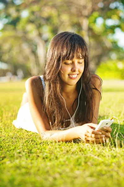 Jonge vrouw luisteren naar muziek op haar mobiele telefoon of speler in park — Stockfoto