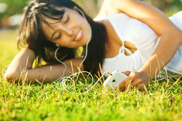 Ung kvinna lyssna på musik på sin mobiltelefon eller spelaren i park — Stockfoto