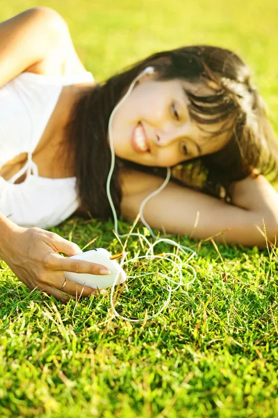 Ung kvinna lyssna på musik på sin mobiltelefon eller spelaren i park — Stockfoto