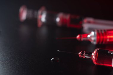 Siyah arka plan ve kırmızı ışıkta cam şırıngaların yakın görüntüsü. Tıp ve sağlık konsepti. Virüslere karşı aşı. İğne ve uyuşturucu. Seçici odaklanma. Boşluğu kopyala