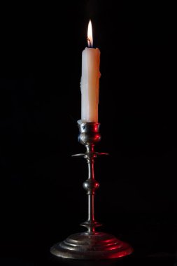 Yanan beyaz mum. Eski metal bir şamdanın üzerinde duruyor. Siyah arka plan. Klasik tarz konsept, dramatik ve gizemli. Dikey fotoğraf.