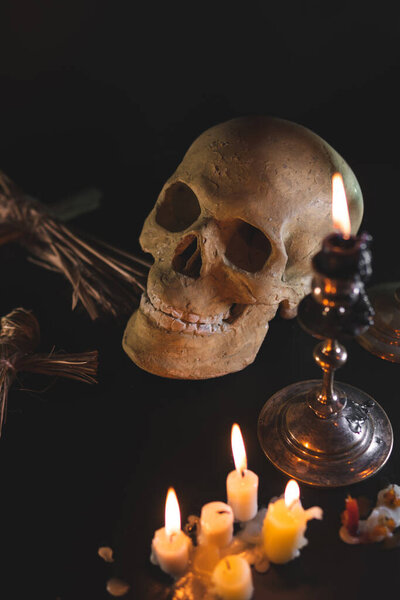 Old Skull and candle with incense on old altar plate which has dim light. Select focus, black background. Straw voodoo dolls. Copy space vertical photo