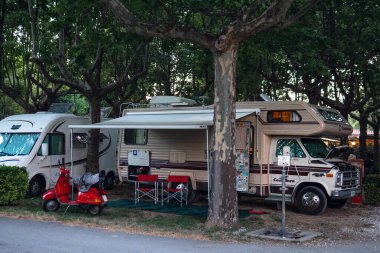 Ameglia, La Spezia, İtalya - 5 Temmuz 2019: Chevrolet Chevy Kamp Van RV Karavanı halka açık bir park River Village Kamp alanı üzerine park edilmiş. Hiç kimse. Kırmızı Vespa motosikleti.