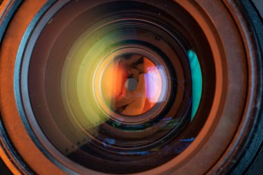 Professional camera photo lens. Details of glass, aperture petals. Light reflections from modern diode lamps. The concept of making visual content. Warm, orange colors