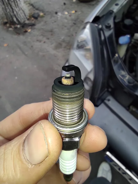 Car spark plug in hands. Poor fuel mixture, soot deposits on the electrode, incorrect engine operation, possible breakdown. Close up. Vertical photo