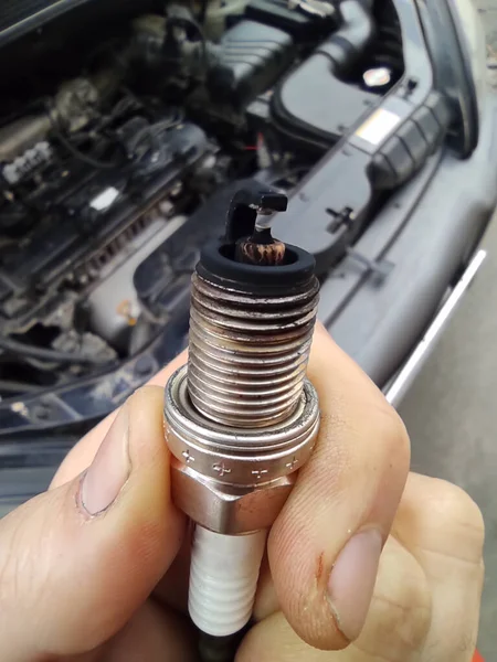 Car spark plug in hands. Poor fuel mixture, soot deposits on the electrode, incorrect engine operation, possible breakdown. Close up. Vertical photo