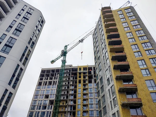 Apartment buildings on sky background. Construction, work on the insulation of the facade with mineral wool. Crane with an arrow. Elevator for high-altitude work. Windows.