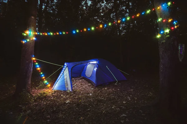 Kampta bir gece. Ormanda renkli fenerleri olan mavi bir çadır. Seyahat ve vahşi doğada tatil. Sandalyeler ve barbekü. Hiç kimse. Boşluğu kopyala