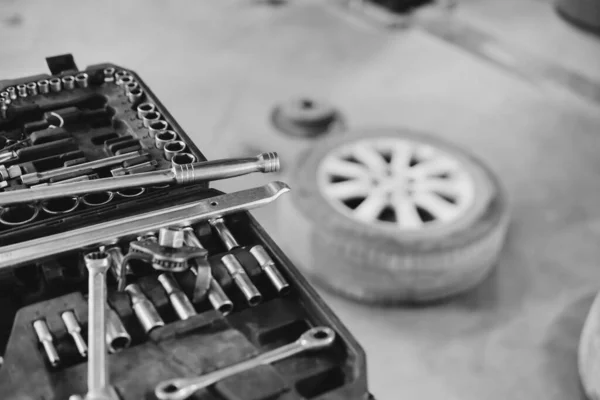 Close up, car repair tool. Car service center. Vehicle raised on lift at maintenance station. Auomobile repair and check up. Wheel. Selective focus. Black and white.