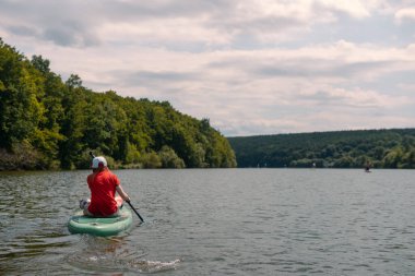The girls sitting on the the SUP board. Big river, lake. Woman surfer in red t-shirt. Reacreation. Paddleboard Water Active lifestyle. Holidays Vacation.