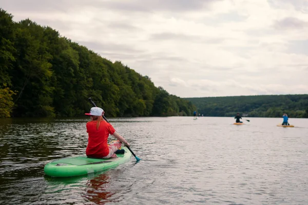 The girls sitting on the the SUP board. Big river, lake. Woman surfer in red t-shirt. Reacreation. Paddleboard Water Active lifestyle. Holidays Vacation.